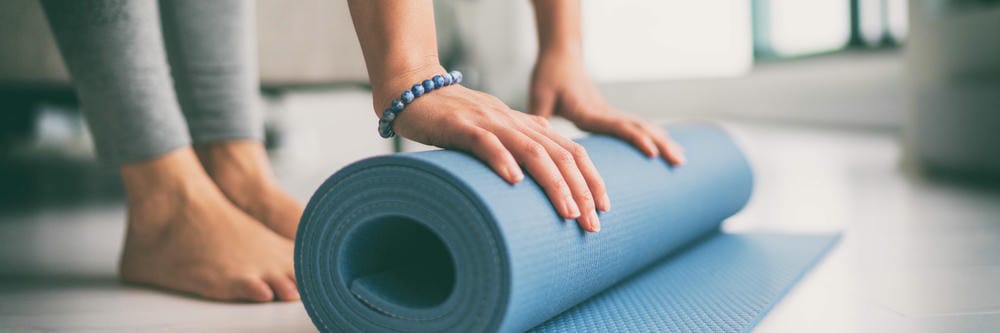 Yoga at home active lifestyle woman rolling exercise mat in living room for morning meditation yoga